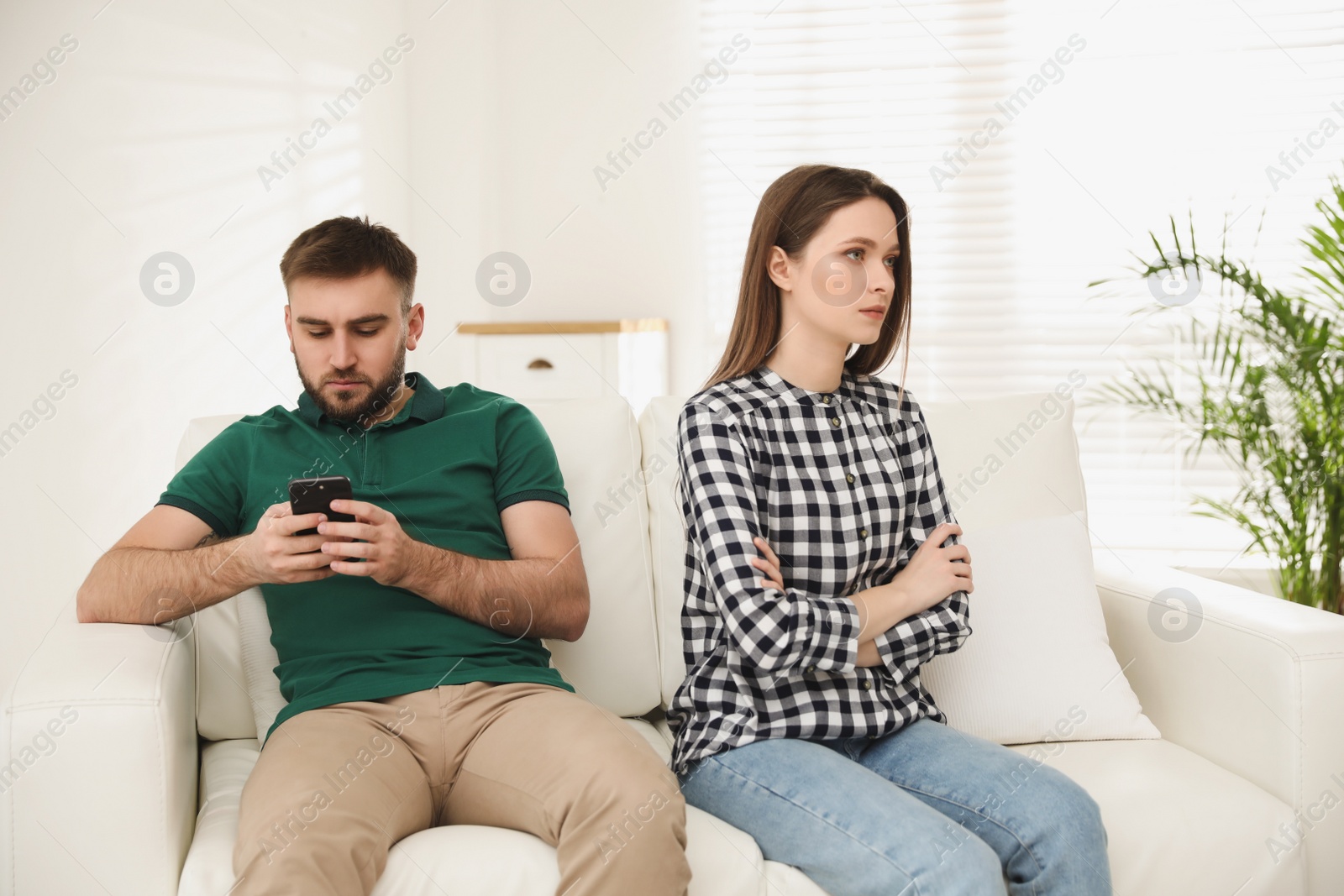 Photo of Young man preferring smartphone over his girlfriend at home. Relationship problems