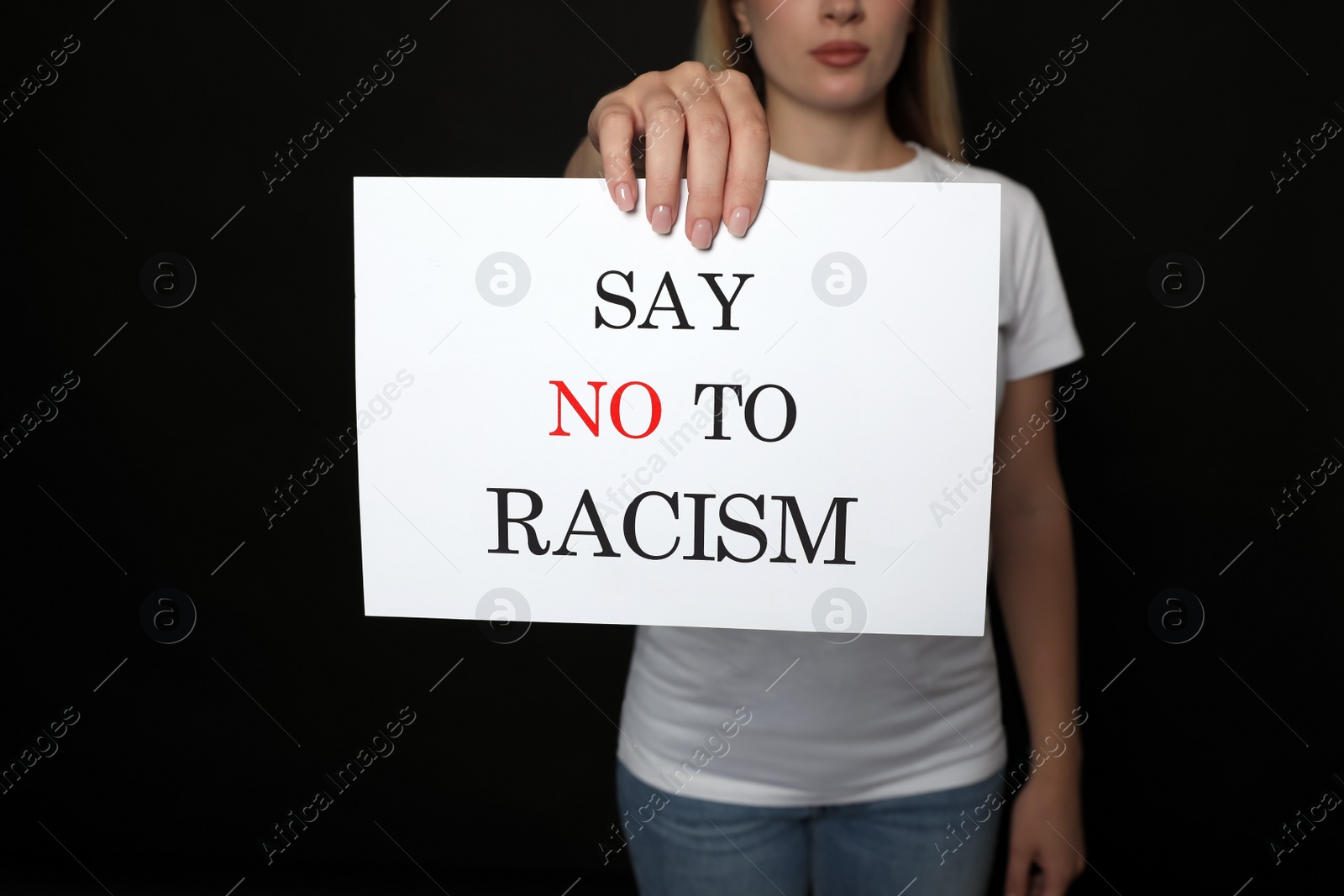 Photo of Young woman holding sign with phrase Say No To Racism on black background, closeup