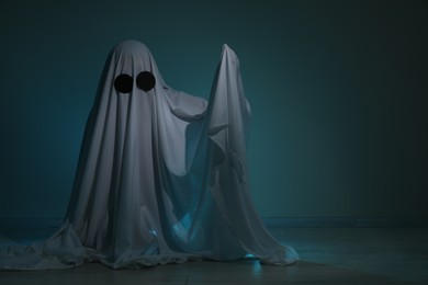 Photo of Creepy ghost. Woman covered with sheet on dark teal background, space for text