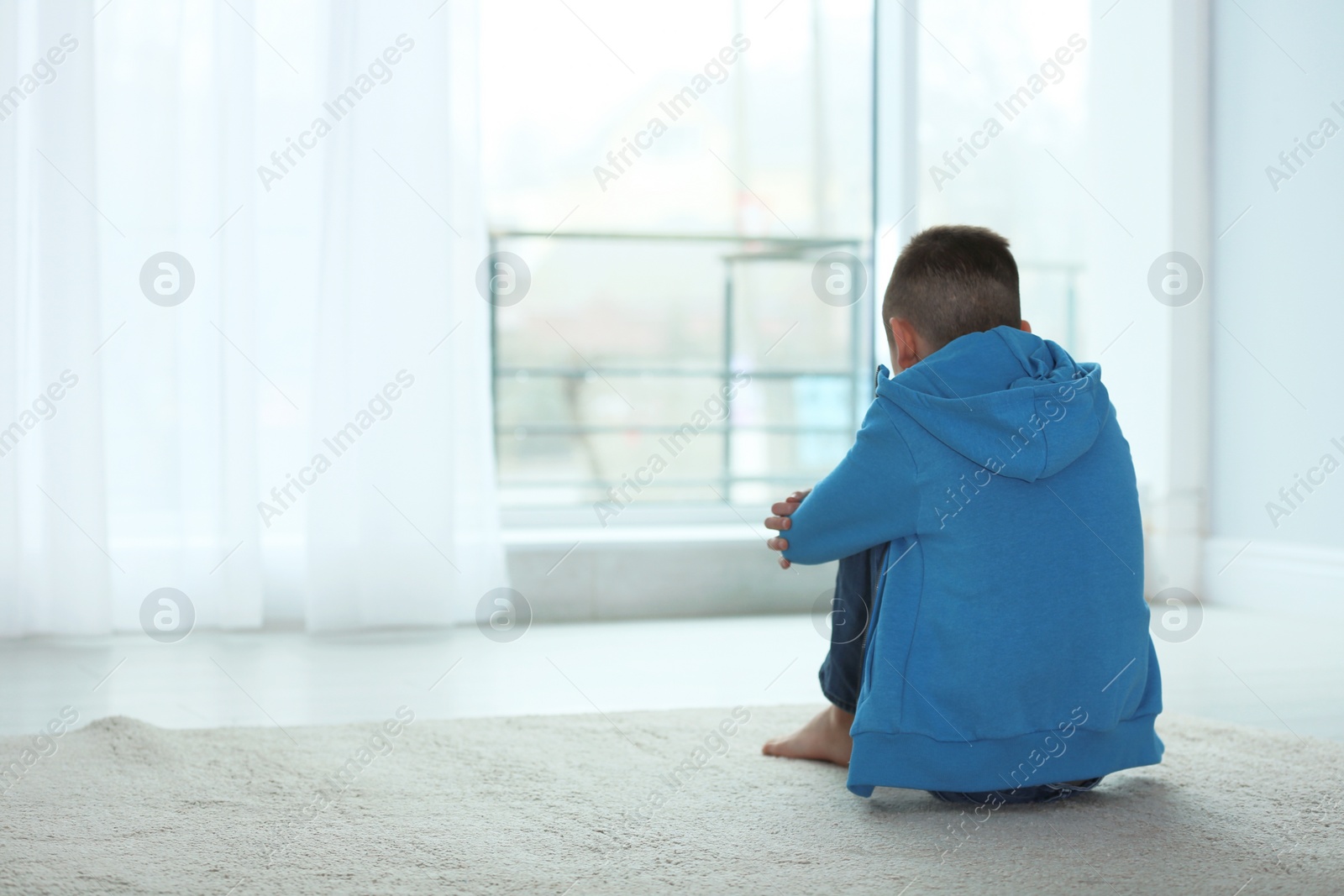 Photo of Upset boy sitting near window indoors. Space for text