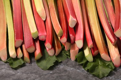 Photo of Many ripe rhubarb stalks and leaves on dark table, closeup