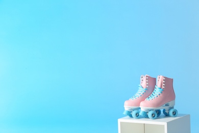 Pair of vintage roller skates on storage cube against color background. Space for text