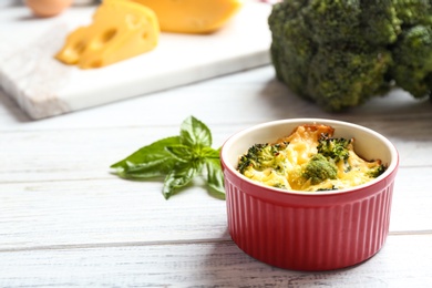 Photo of Tasty broccoli casserole in ramekin on white wooden table