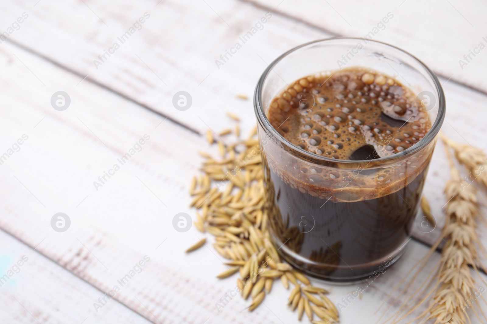 Photo of Cup of barley coffee, grains and spike on white wooden table, closeup. Space for text