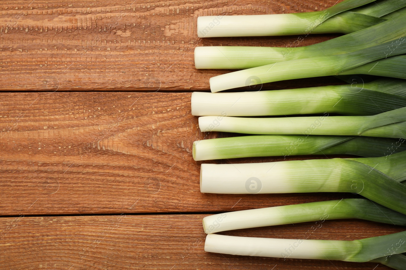 Photo of Fresh raw leeks on wooden table, flat lay. Space for text