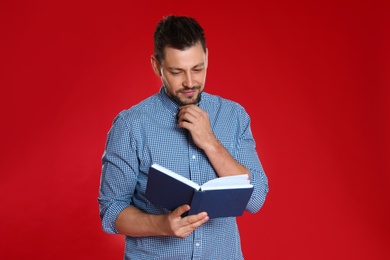 Photo of Handsome man reading book on red background