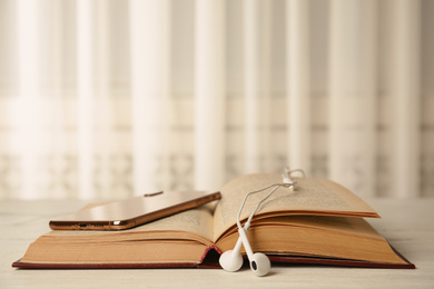 Open book, earphones and mobile phone on white wooden table