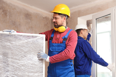 Photo of Workers in uniform installing plastic windows indoors