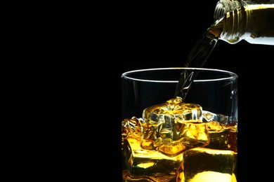 Photo of Pouring whiskey into glass with ice cubes on black background, closeup. Space for text