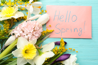 Photo of Pink card with words HELLO SPRING and fresh flowers on light blue wooden table, flat lay