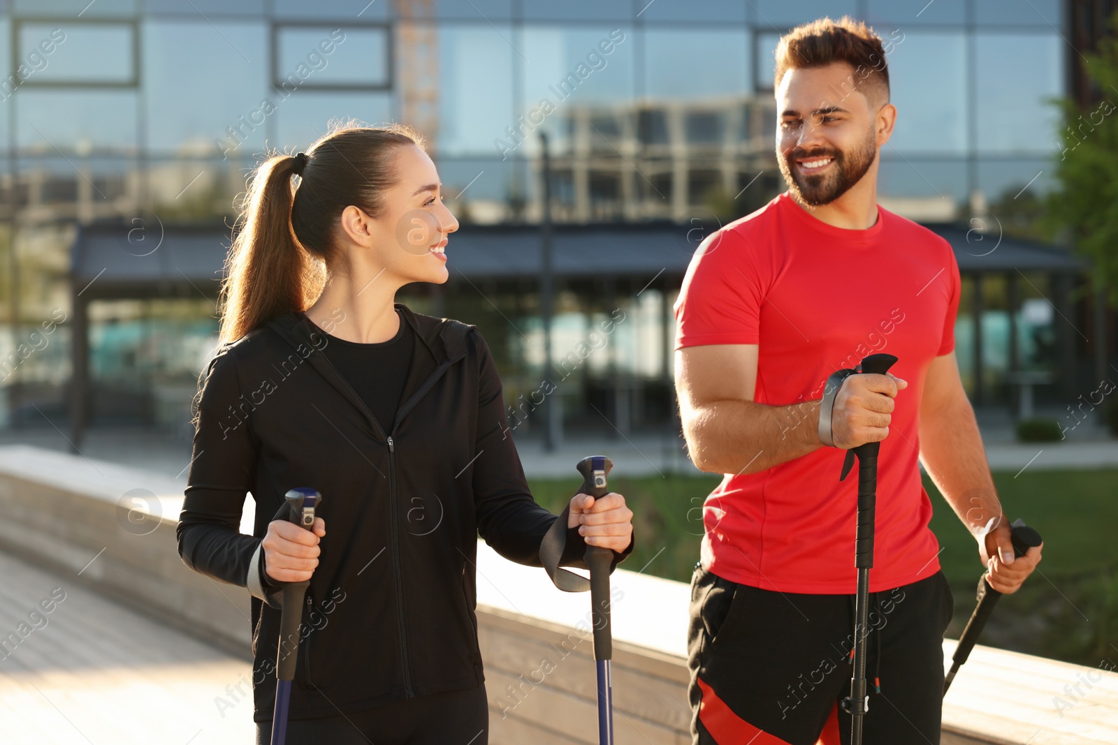 Photo of Happy couple practicing Nordic walking with poles outdoors on sunny day