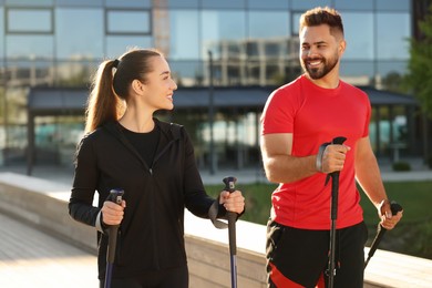 Photo of Happy couple practicing Nordic walking with poles outdoors on sunny day