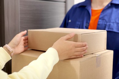 Photo of Courier giving parcels to woman indoors, closeup