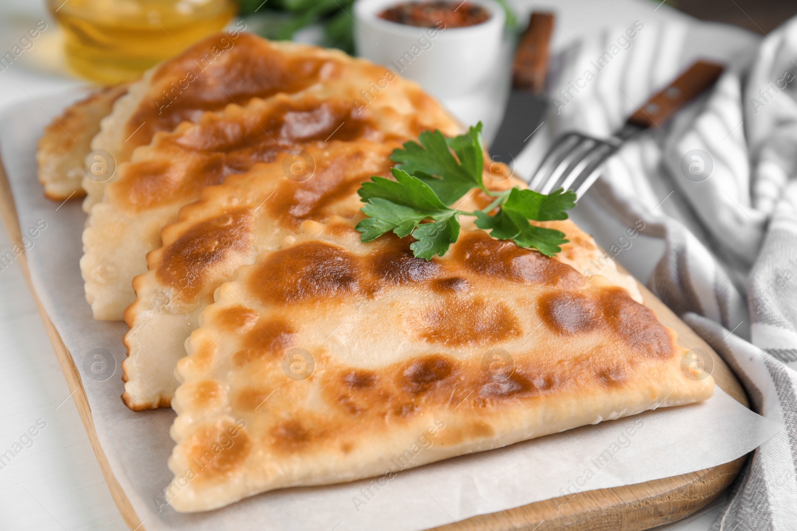 Photo of Board with delicious fried chebureki and parsley on white table, closeup