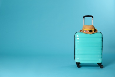 Stylish suitcase with hat and sunglasses on color background. Space for text