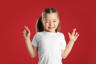 Photo of Child with crossed fingers on red background. Superstition concept