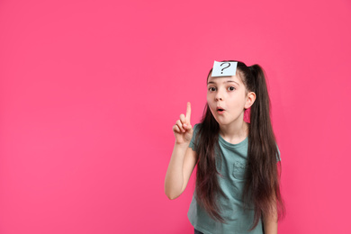 Photo of Emotional girl with question mark sticker on forehead against pink background. Space for text