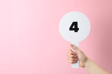 Photo of Woman holding auction paddle with number 4 on pink background, closeup. Space for text