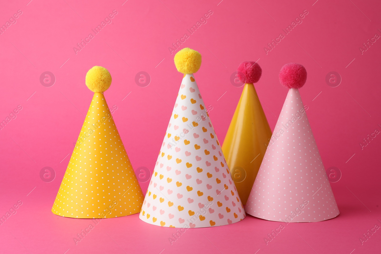 Photo of Beautiful party hats with pompoms on pink background