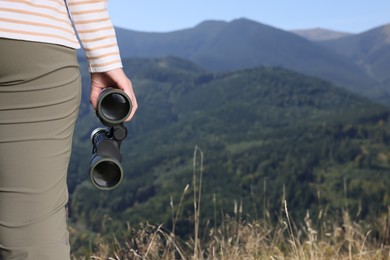 Woman with binoculars in mountains on sunny day, closeup