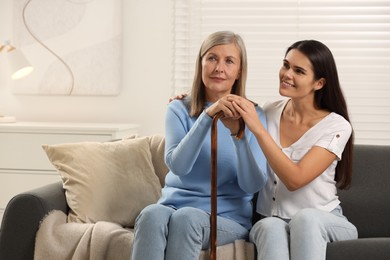 Mature lady with walking cane and young woman on sofa at home