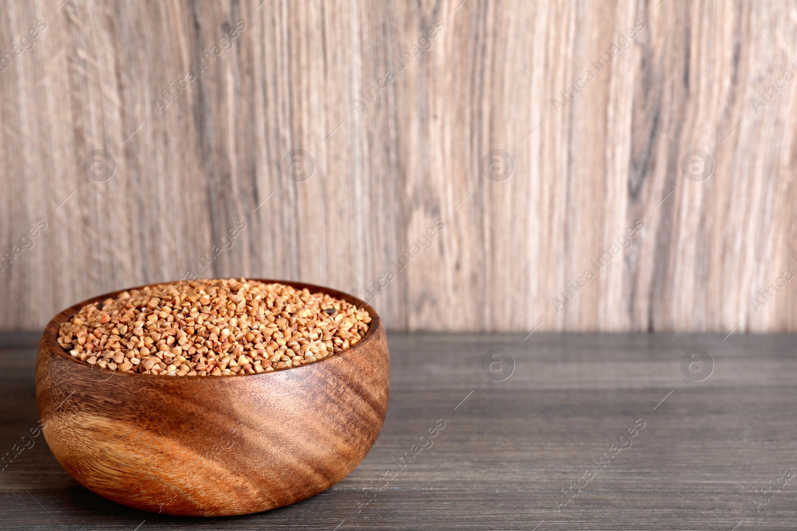 Photo of Uncooked buckwheat in bowl on wooden table. Space for text