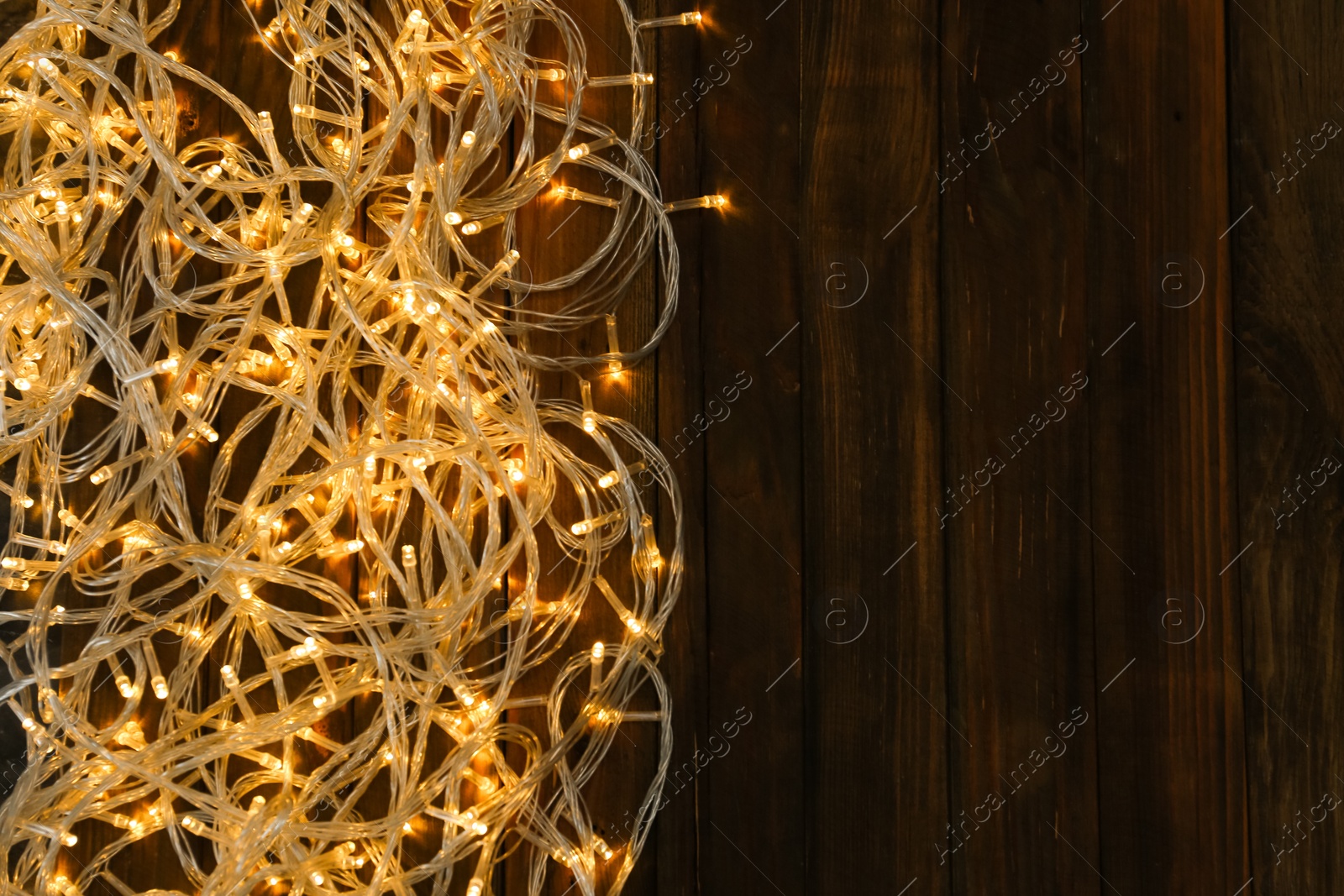 Photo of Glowing Christmas lights on wooden background, top view. Space for text