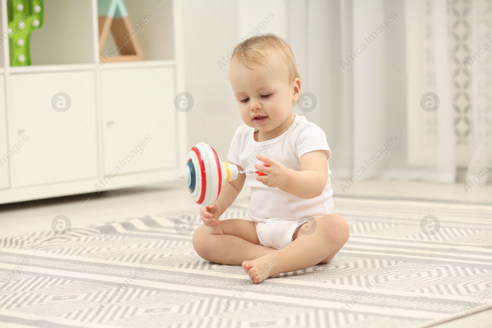 Photo of Children toys. Cute little boy playing with spinning top on rug at home