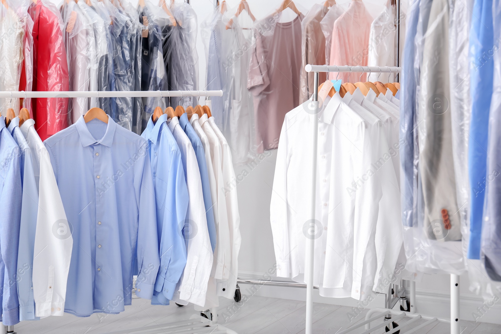 Photo of Racks with clean clothes on hangers after dry-cleaning indoors