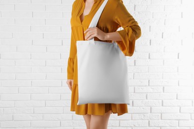 Photo of Woman with white textile bag near brick wall, closeup. Space for design