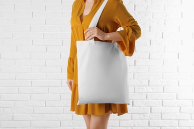 Woman with white textile bag near brick wall, closeup. Space for design