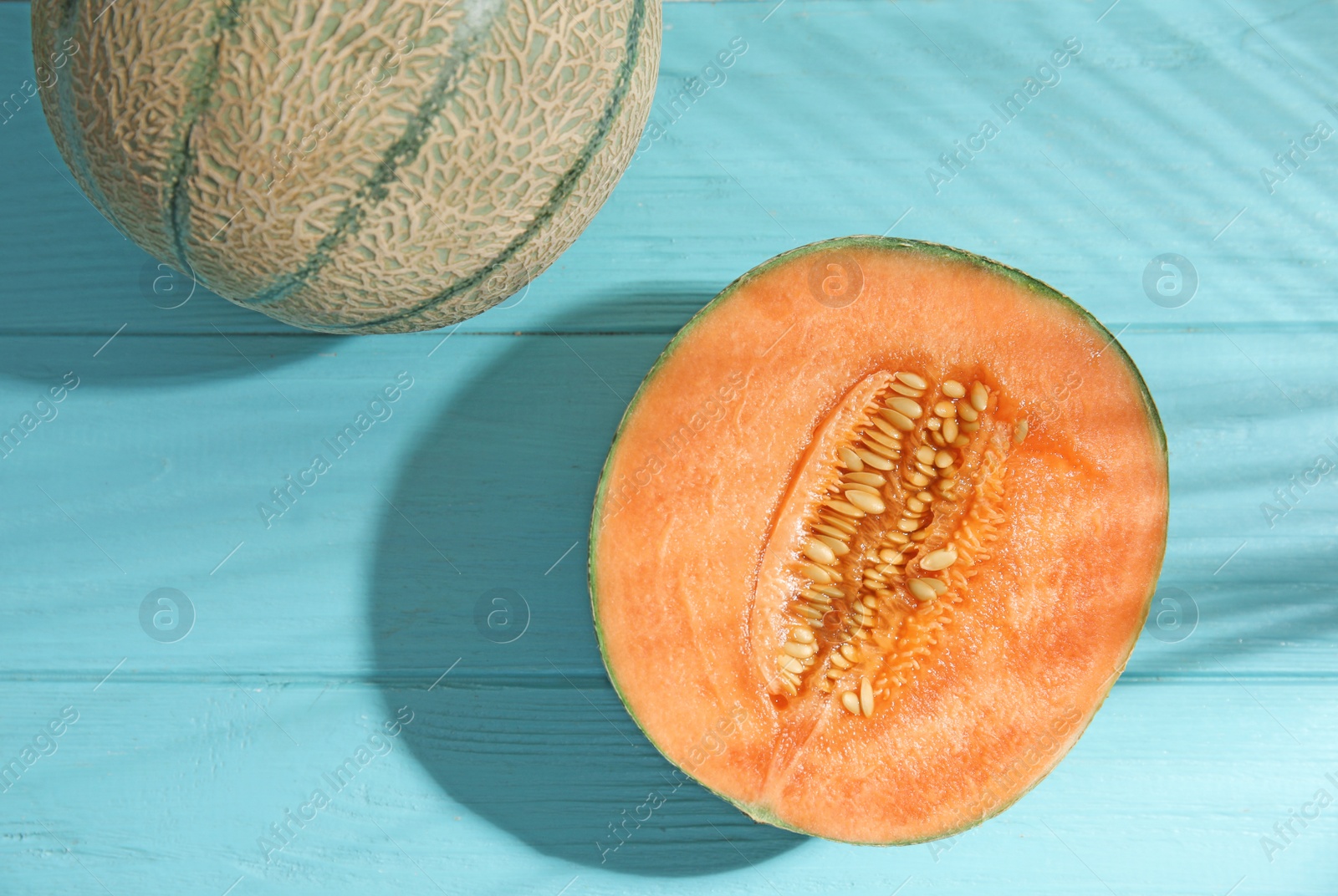 Photo of Tasty ripe cantaloupe melons and palm leaf shadow on light blue wooden table, flat lay