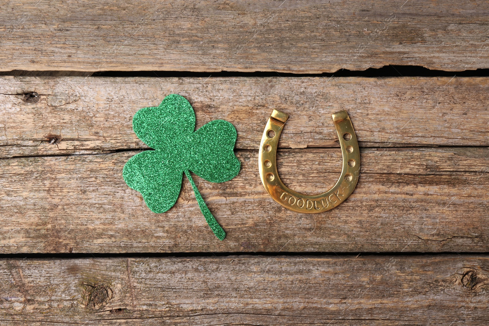 Photo of St. Patrick's day. Golden horseshoe and green decorative clover leaf on wooden table, flat lay