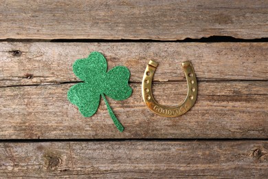 Photo of St. Patrick's day. Golden horseshoe and green decorative clover leaf on wooden table, flat lay