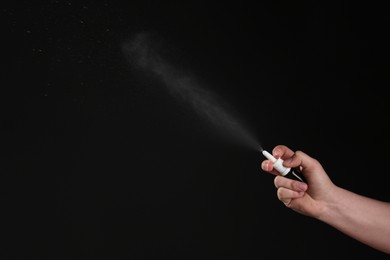 Photo of Nasal congestion. Woman spraying remedy from bottle on black background, closeup with space for text
