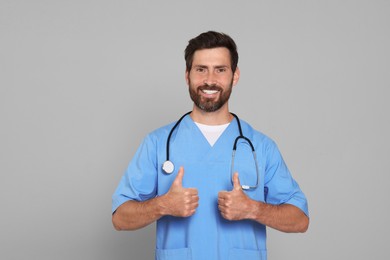 Doctor with stethoscope showing thumbs up on light grey background