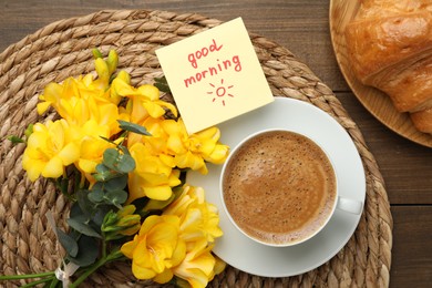Photo of Cup of aromatic coffee with croissant, beautiful yellow freesias and Good Morning note on wooden table, flat lay