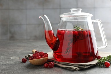 Photo of Tasty hot cranberry tea in teapot, rosemary and fresh berries on light grey textured table