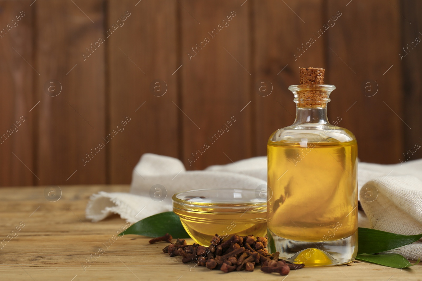 Photo of Essential oil and dried cloves on wooden table. Space for text