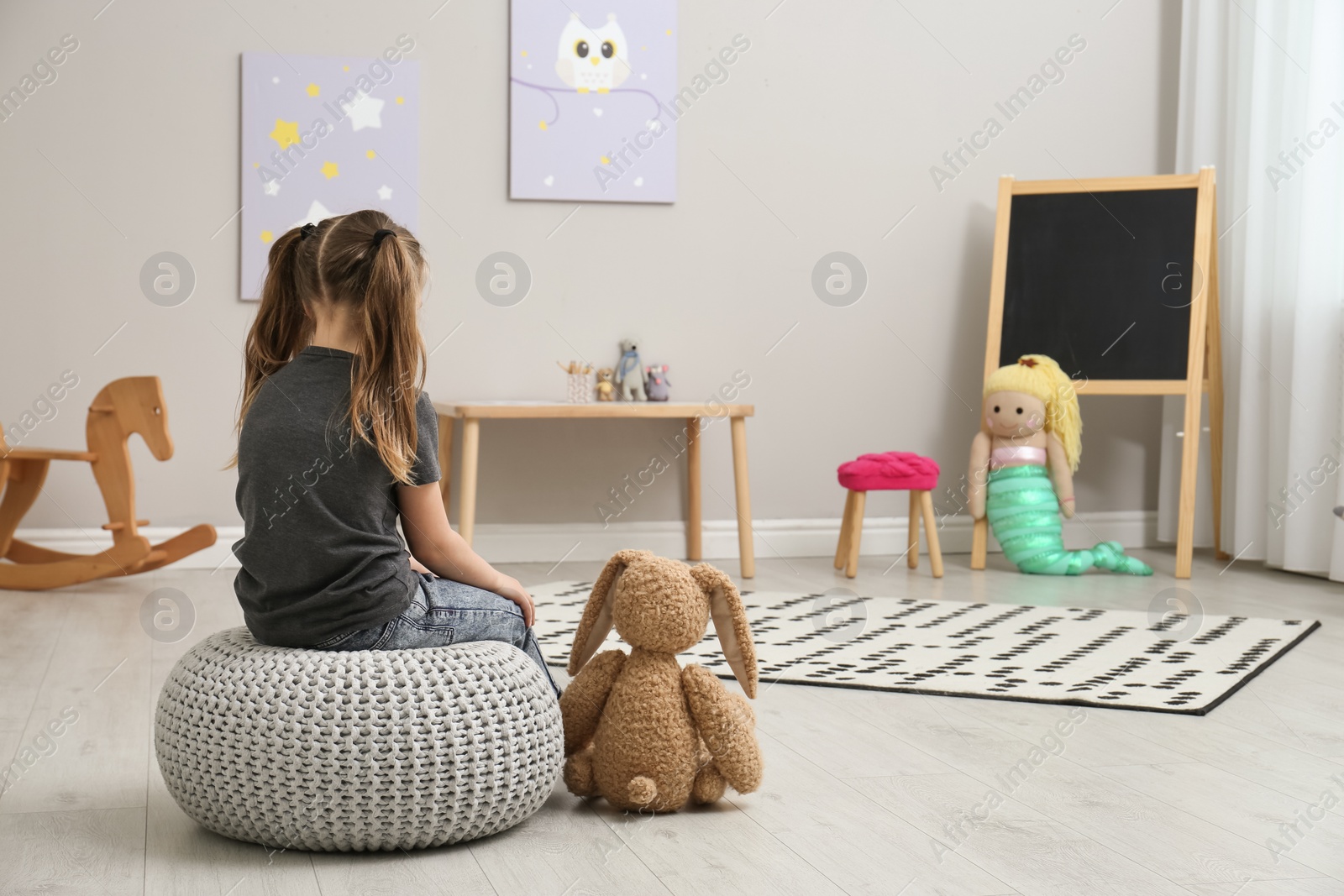 Photo of Lonely little girl with toy bunny at home, back view. Autism concept