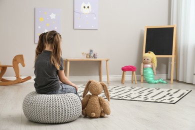 Lonely little girl with toy bunny at home, back view. Autism concept