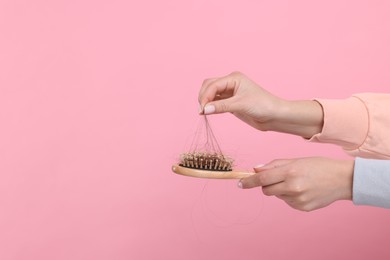 Photo of Woman untangling her lost hair from brush on pink background, closeup and space for text. Alopecia problem