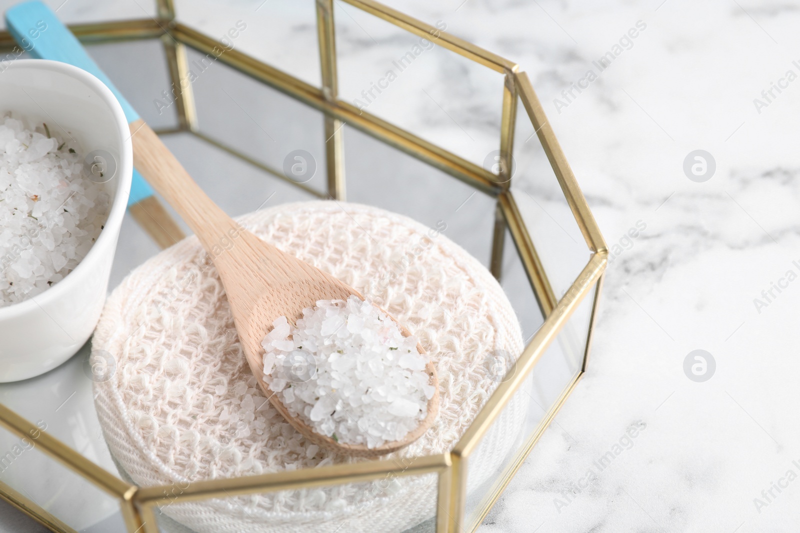 Photo of Wooden spoon with sea salt for spa scrubbing procedure on white marble table