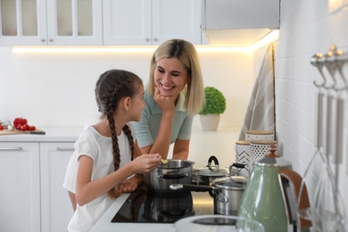 Photo of Little girl with her mother cooking together in modern kitchen