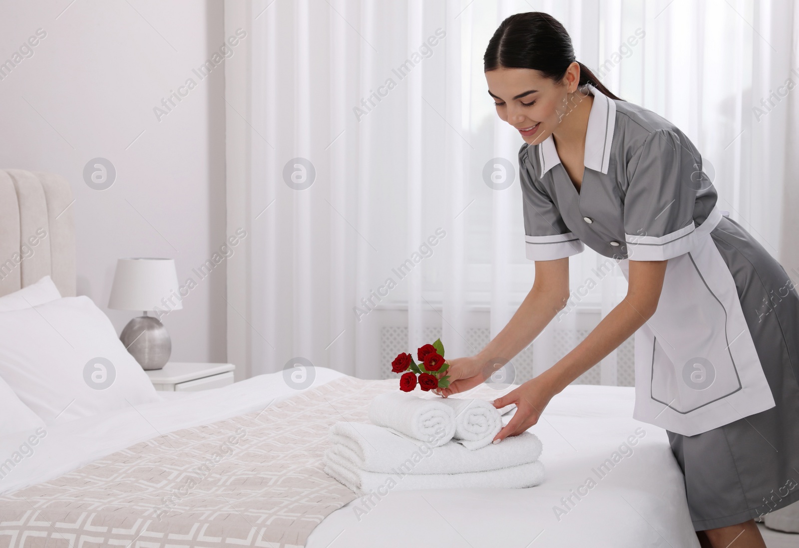 Photo of Chambermaid putting flowers with fresh towels in hotel room. Space for text