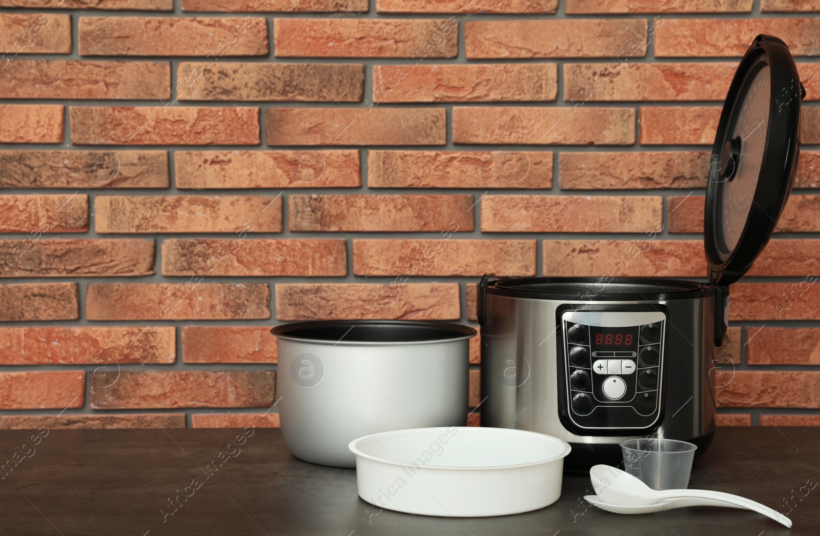 Photo of Modern electric multi cooker, parts and accessories on table near brick wall. Space for text