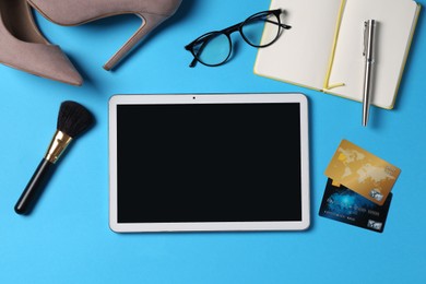 Online store. Tablet, stationery, credit cards, glasses, brush and shoes on light blue background, flat lay