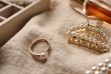 Photo of Elegant hair clip and ring with pearls on beige fabric, closeup
