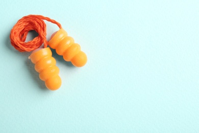Photo of Pair of orange ear plugs with cord on turquoise background, top view. Space for text