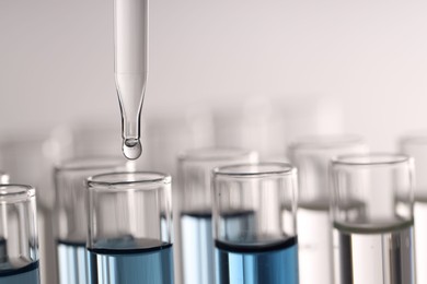 Dripping liquid from pipette into test tube on light background, closeup